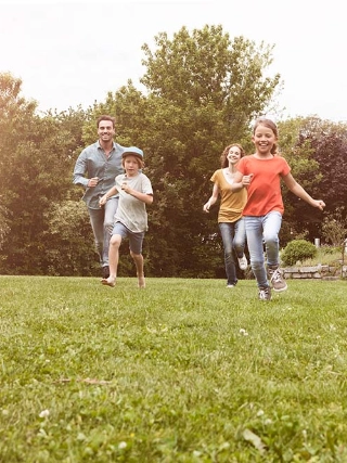 Eine glueckliche Familie mit zwei Kindern spielt im Garten vor ihrem Eigenheim.